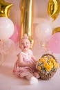 Baby Girl in Pink Dress Sitting on Floor with Basket of Flowers