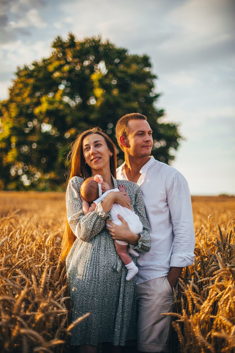 Couple With Their Newborn Baby On A Field 