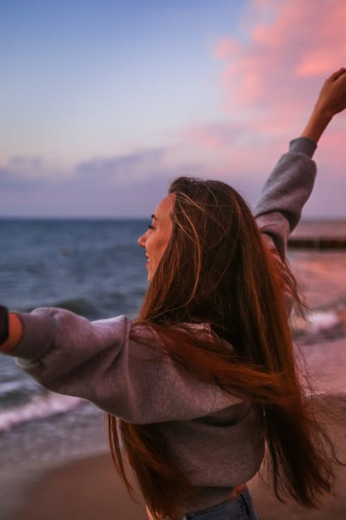 Smiling Woman Spreading Her Arms and Facing the Sea at Sunset 