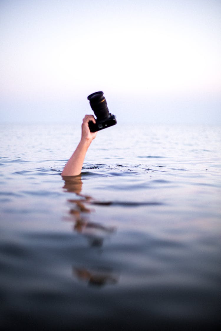 Persons Hand Emerging From Water Holding A Camera 