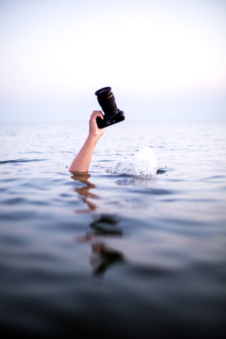 Person's Hand Emerging From Water Holding A Camera 