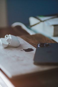 A minimalist desk setup featuring AirPods, smartphone, and laptop in soft focus lighting.