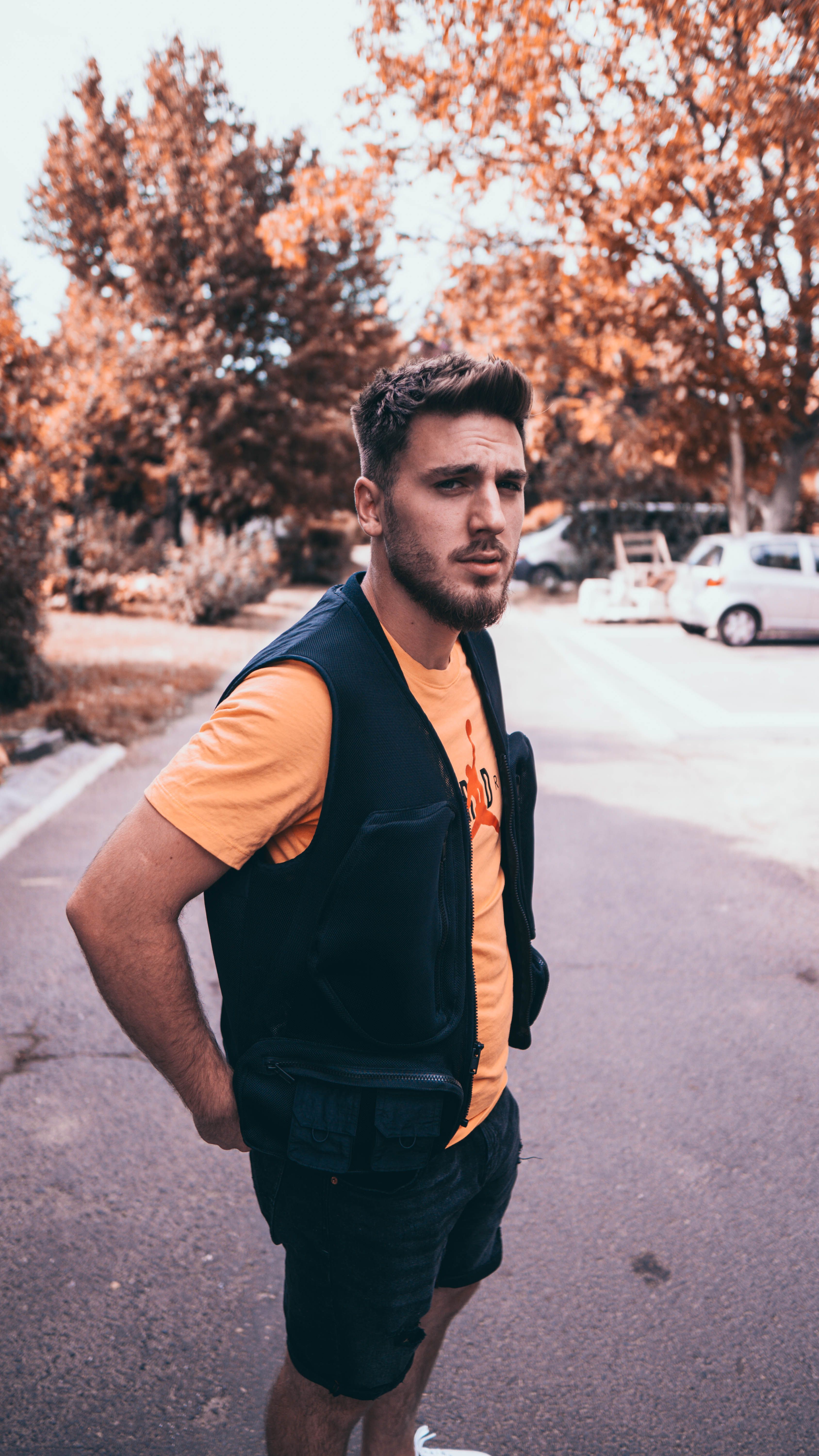 Bearded man standing on a street during a warm autumn day, showcasing casual fashion.