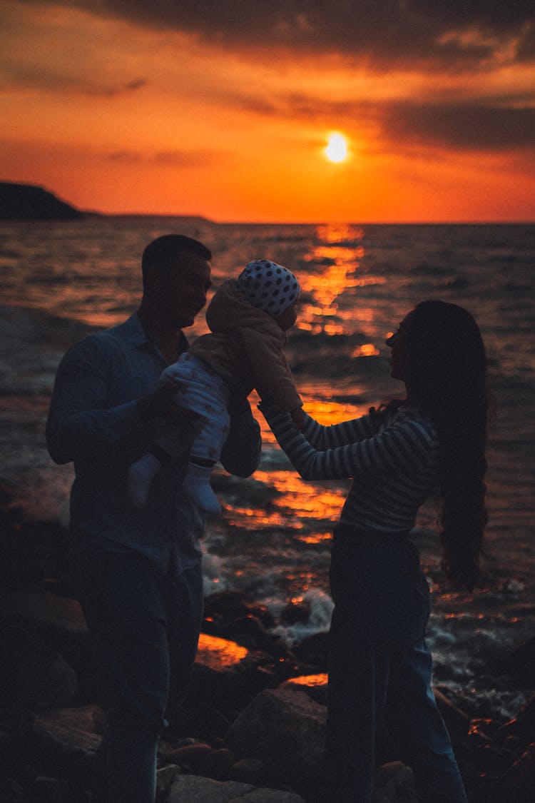 Couple With A Baby On The Beach At Sunset 