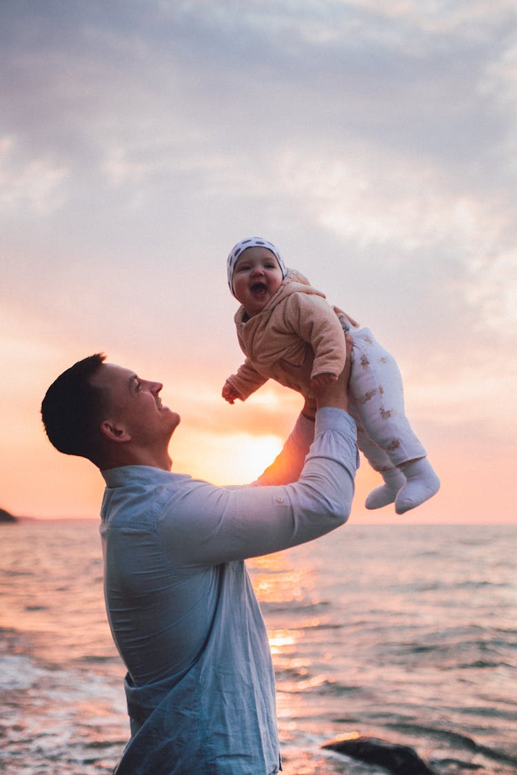 Man Lifting A Baby During Sunset At Sea