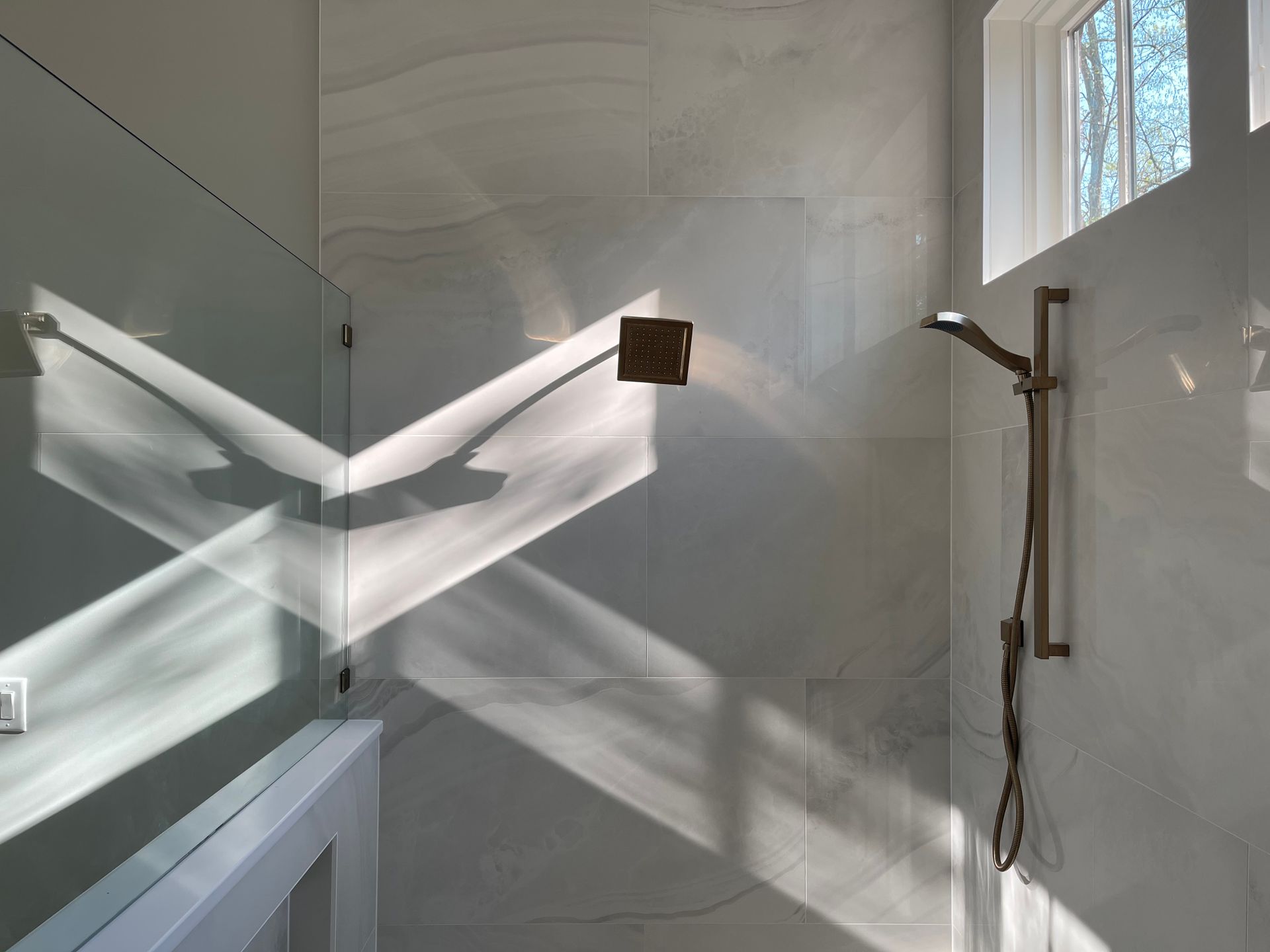Elegant minimalist bathroom showcasing sunlit reflections on marble tiles and shower fixtures.