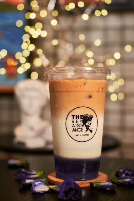 Aesthetic iced coffee exhibited in an art cafe with fairy lights creating a cozy ambiance.