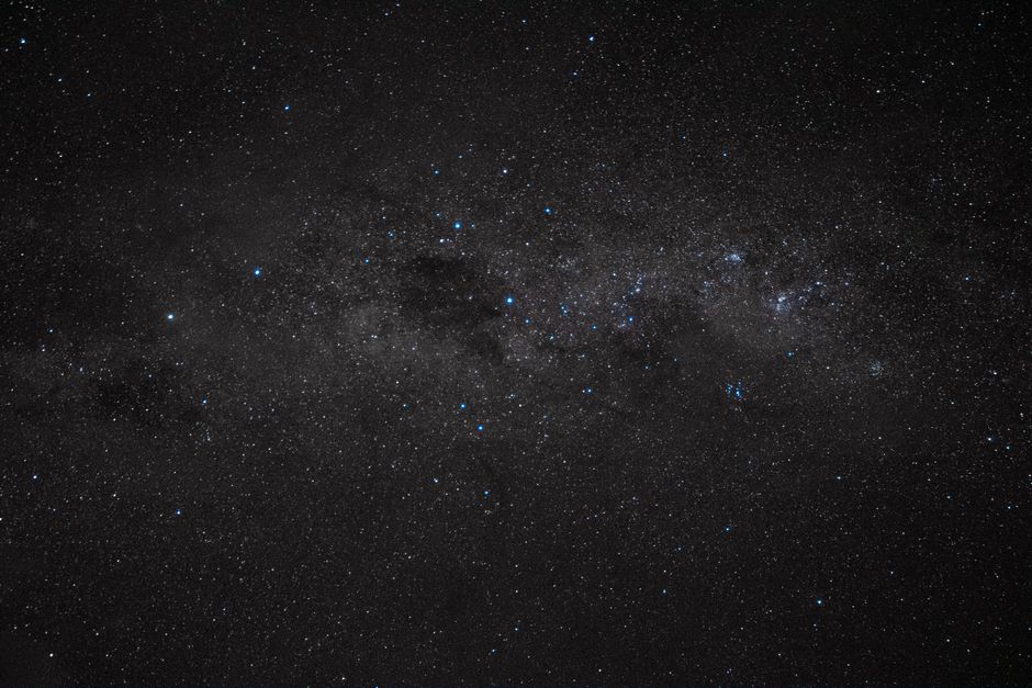 Starry night sky with the Milky Way stretching across, dense star fields visible above a dark horizon