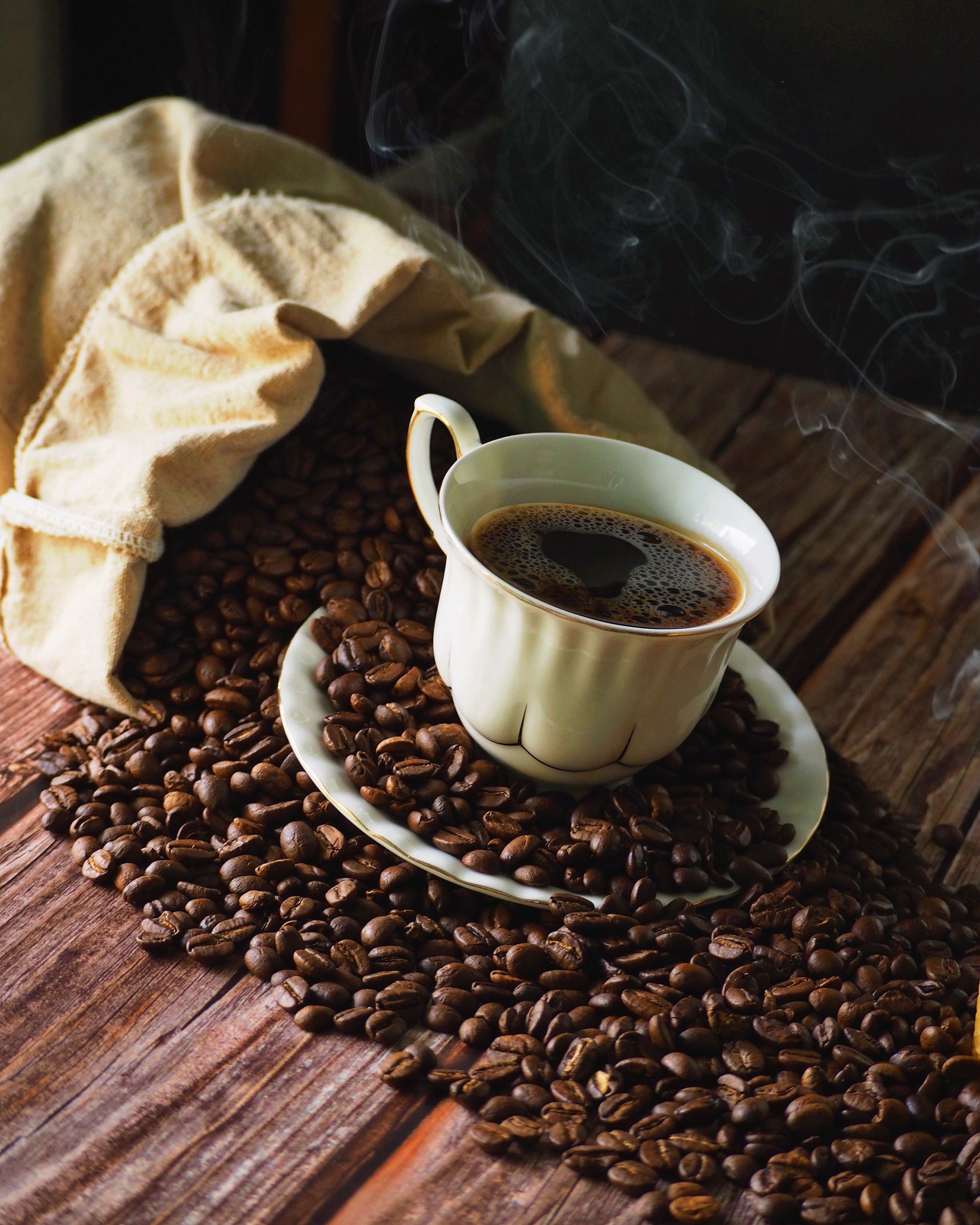 steaming hot coffee in a cup surrounded by coffee beans on a rustic wooden table.