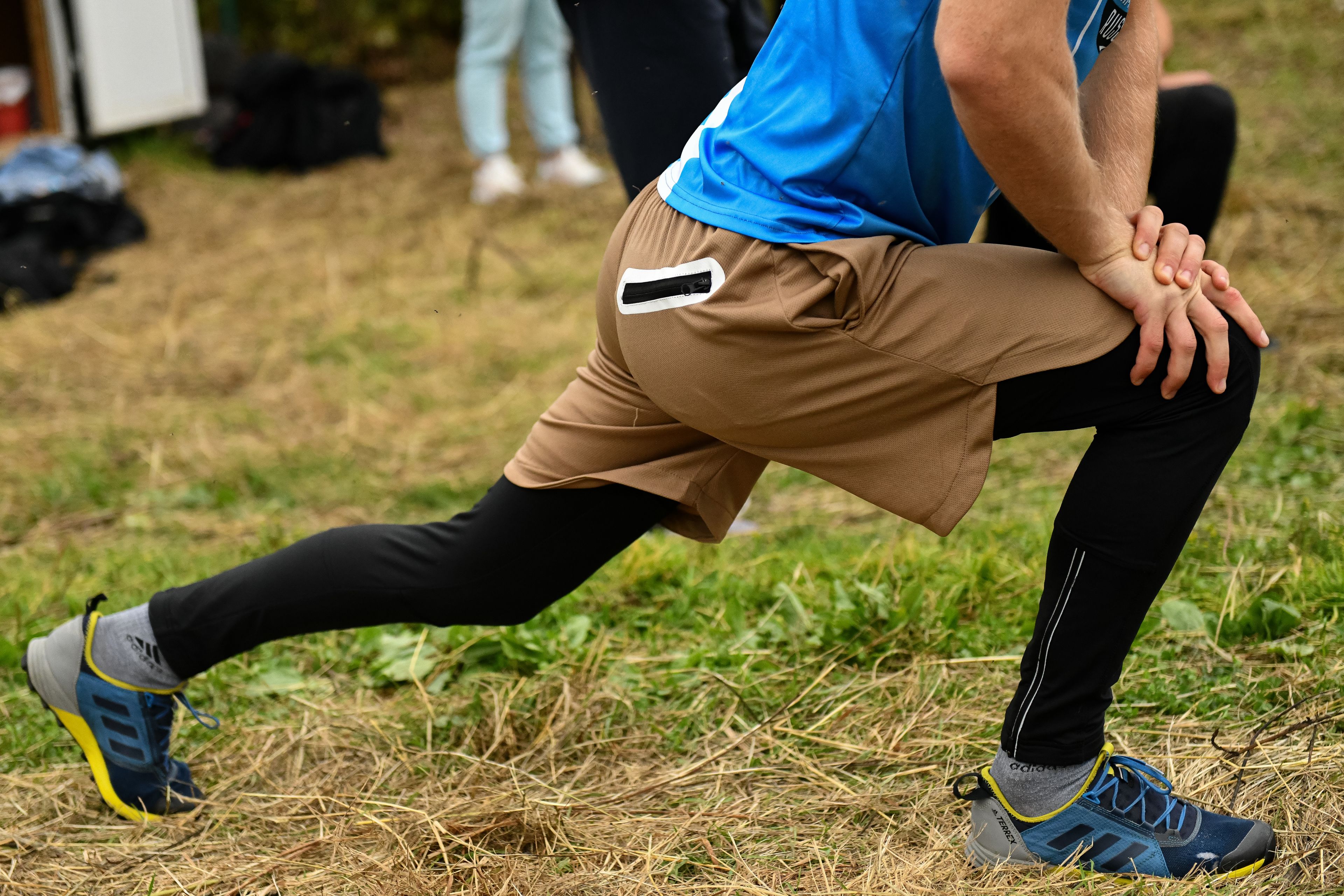 Close-up of a man stretching outdoors in sports attire, focusing on leg muscles and athletic shoes.