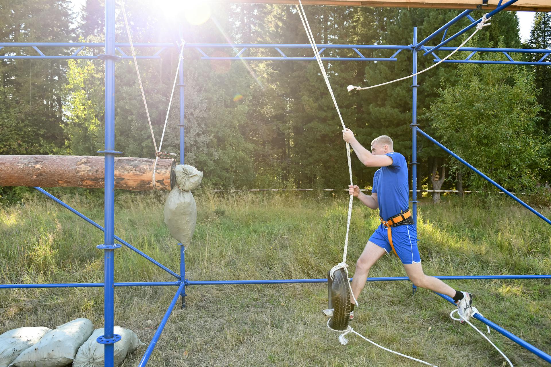 Man in Blue Shirt and Shorts Stepping on a Tire in an Obstacle Course