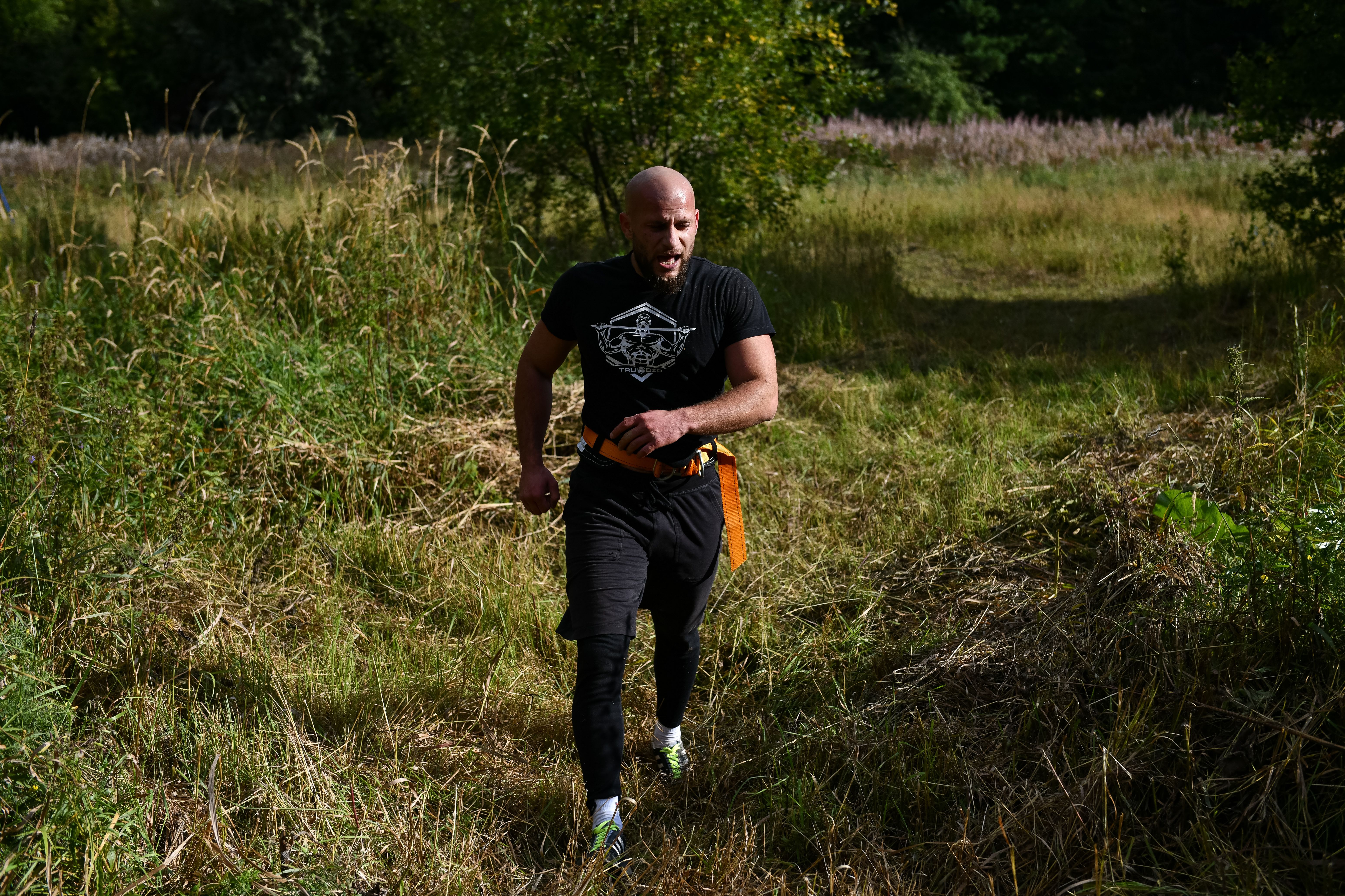 A Man in a Black Shirt Walking on a Field of Grass · Free Stock Photo