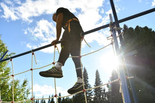 Adult man demonstrating strength on an outdoor climbing net under sunny skies.