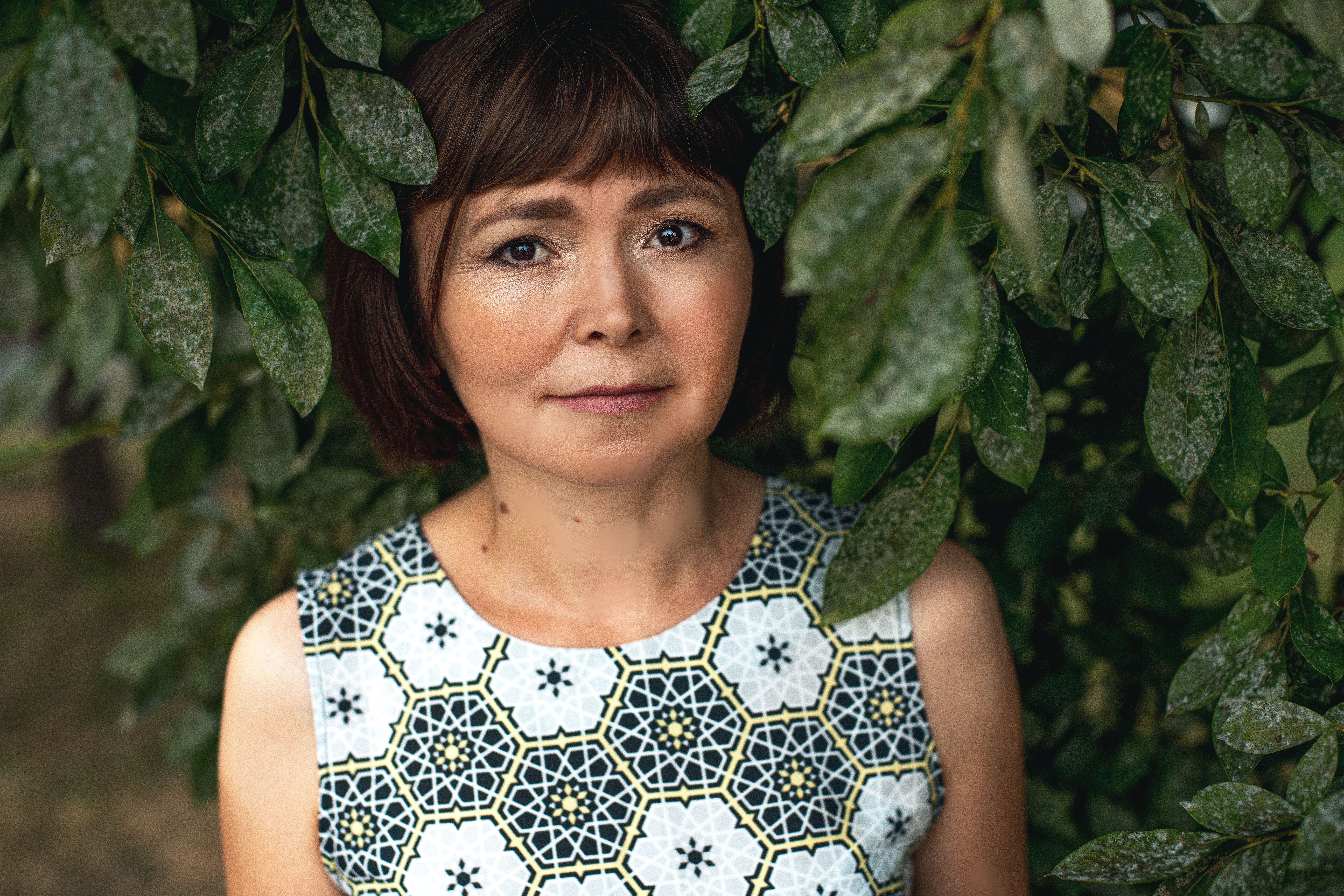 Close-up portrait of a woman surrounded by lush green leaves, exuding a serene expression.