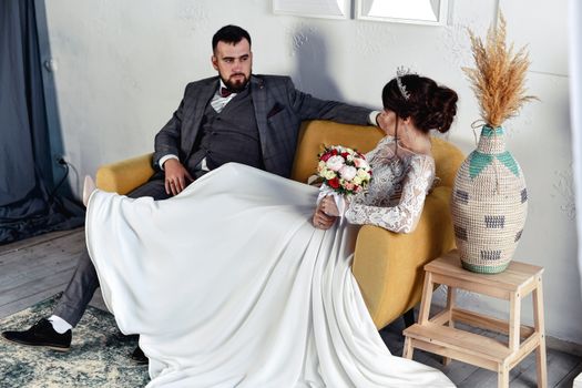 Stylish bride and groom elegantly seated indoors, showcasing wedding fashion with a romantic ambiance.