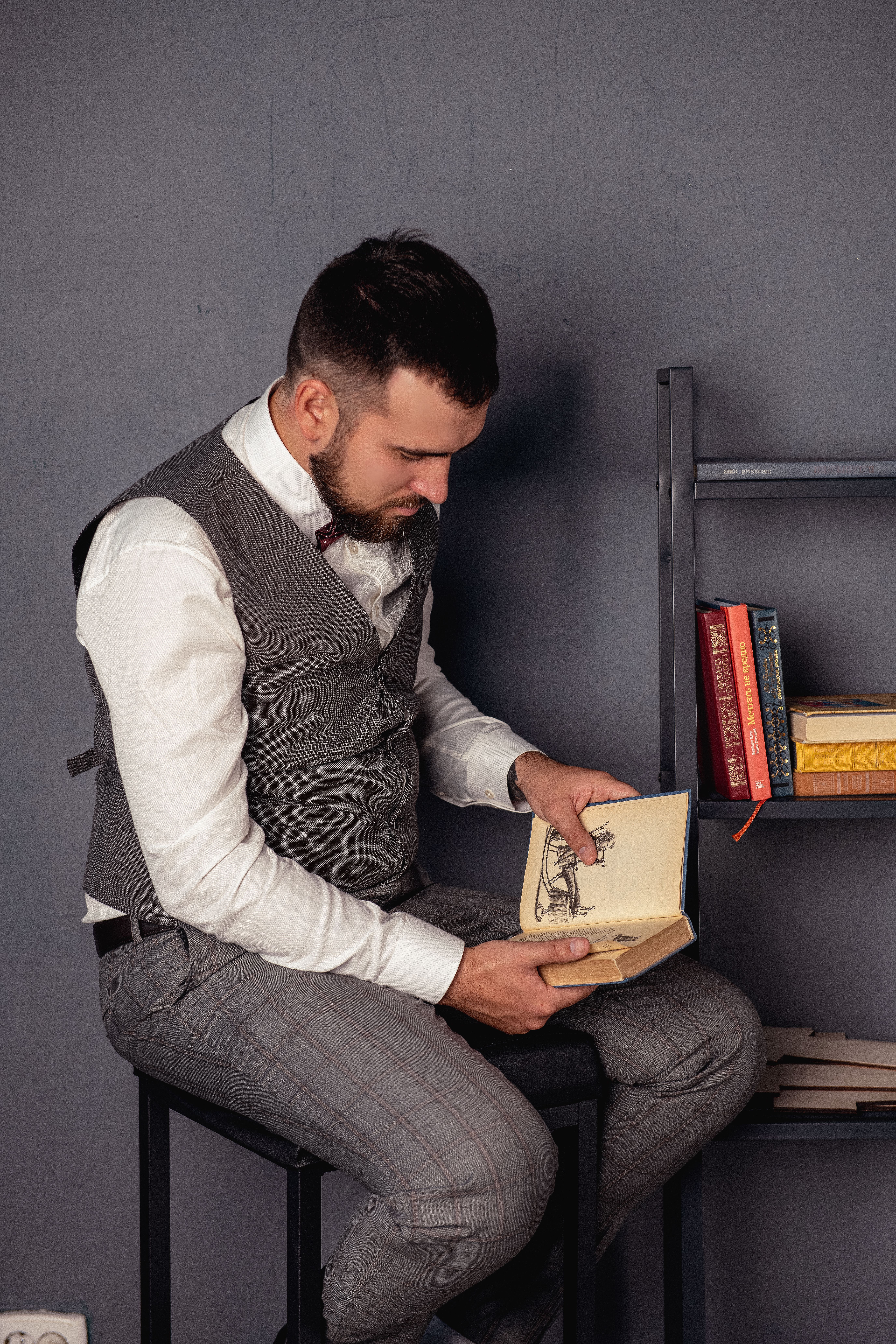 Young man in formal attire reading a book indoors. Relaxed and focused.