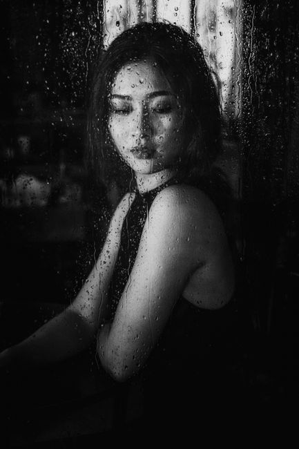 Monochrome portrait of a woman gazing through a rainy window, exuding a moody and introspective vibe.
