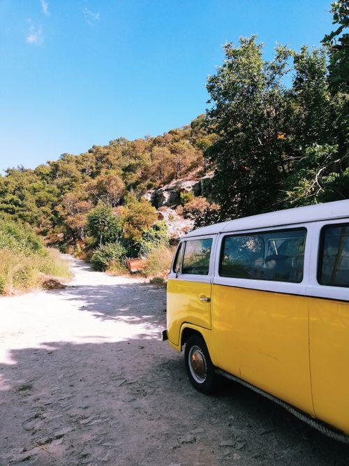Free A classic yellow van parked on a sunlit dirt road surrounded by lush greenery and hills. Stock Photo