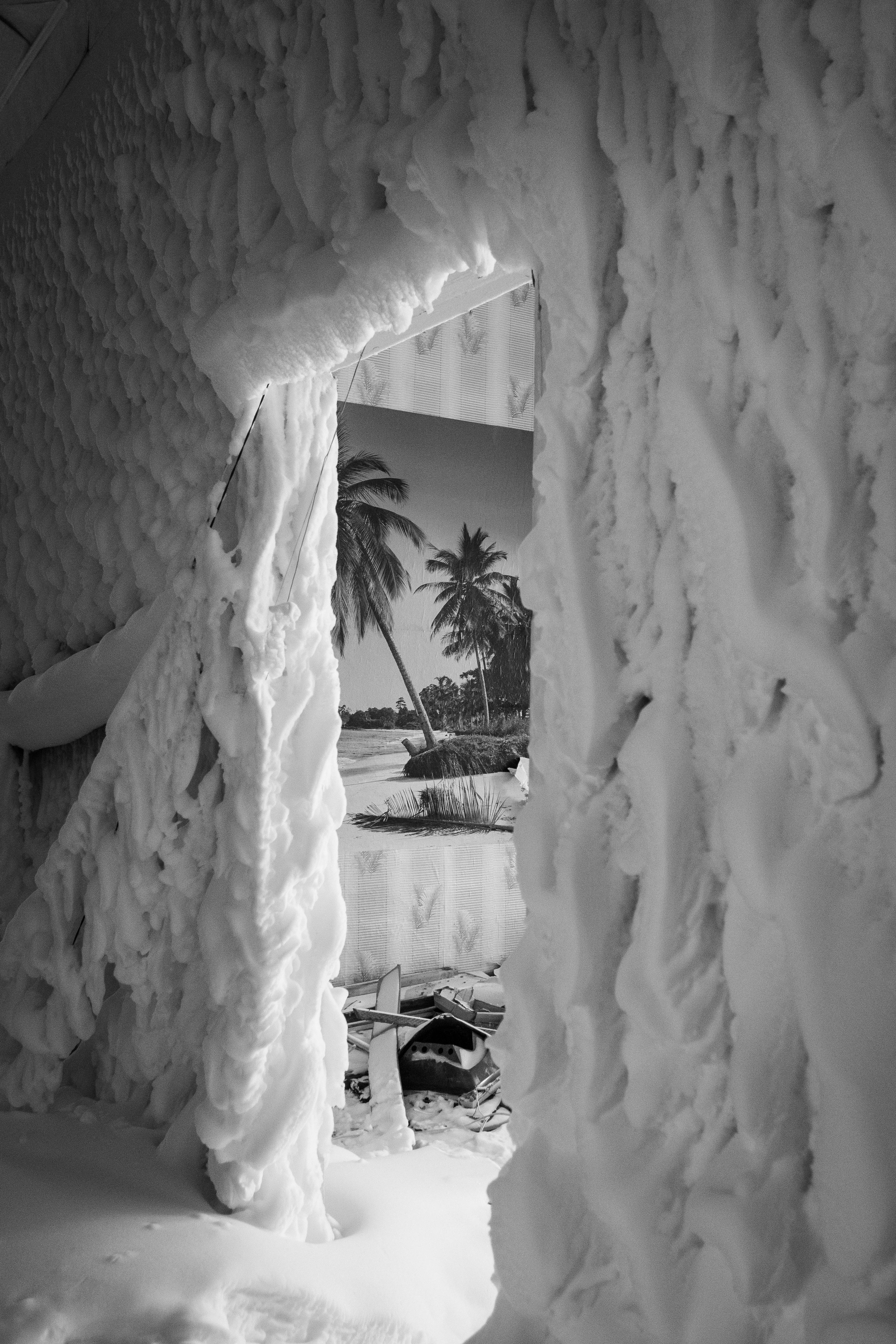 A black and white image of a snow-covered room revealing a tropical poster on a wall.