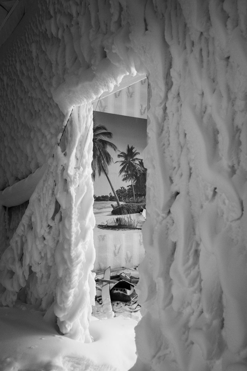 Imagem em preto e branco de um quarto coberto de neve revelando um pôster tropical na parede.