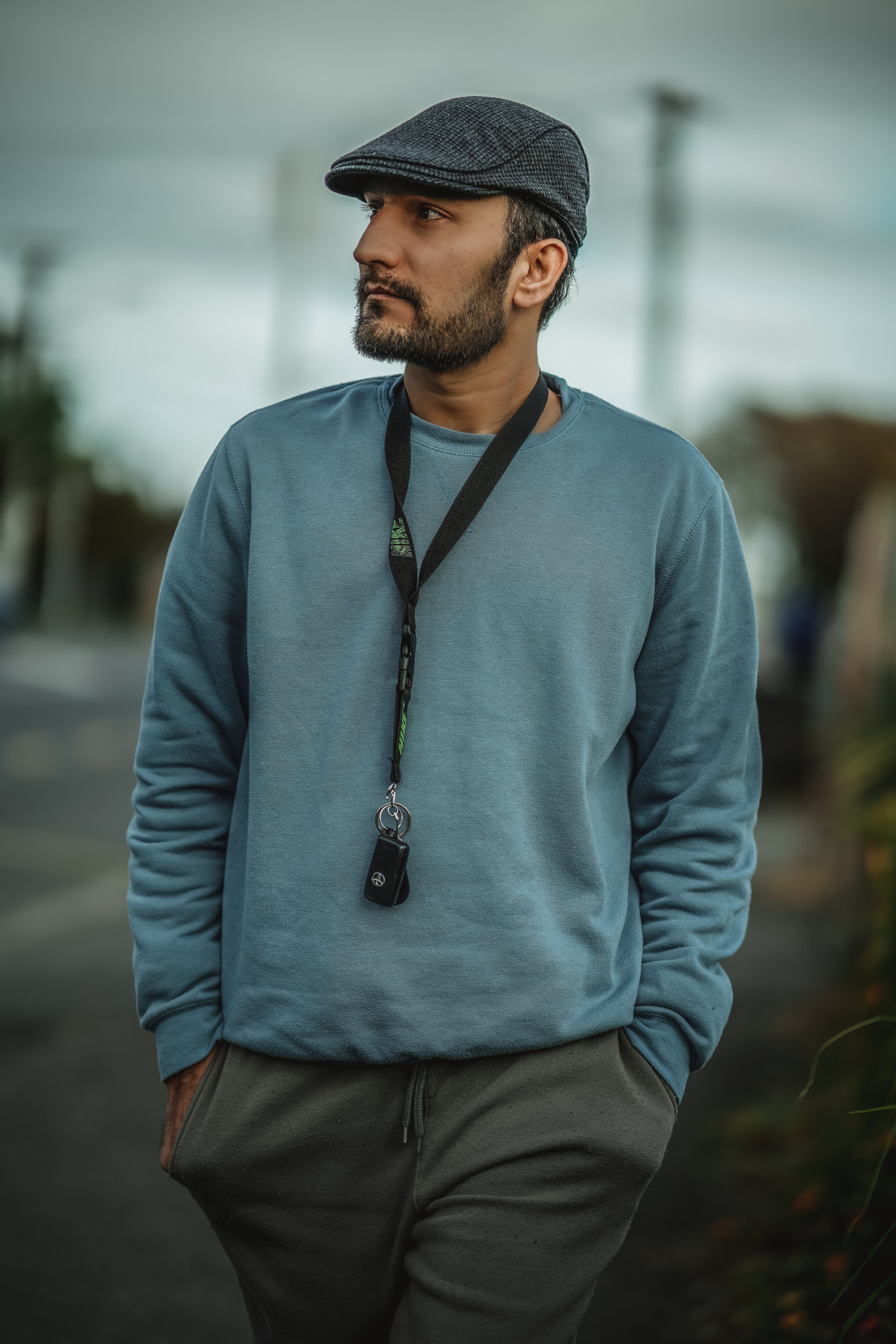 Man wearing a blue sweater and cap, looking pensive outdoors in a natural setting.