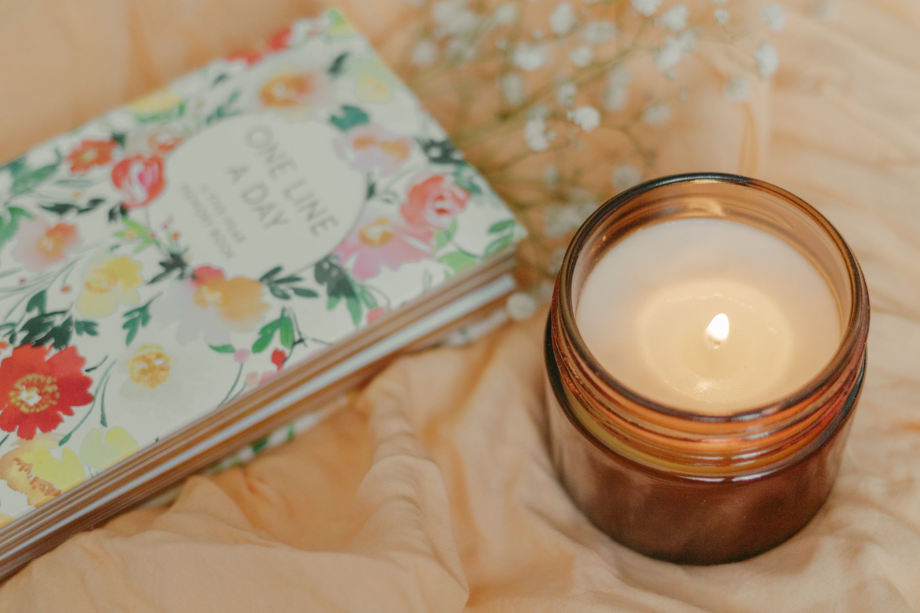 A book beside a candle on soft fabric captures the quieter, slower mood of reflection that memoir asks for once certainty has fallen away.