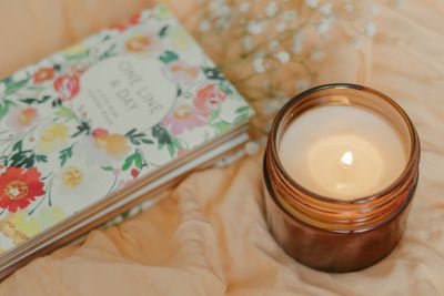 An open notebook beside a lit candle on soft fabric