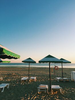 Tranquil beach in Anapa, Russia with green umbrellas and loungers at sunset.
