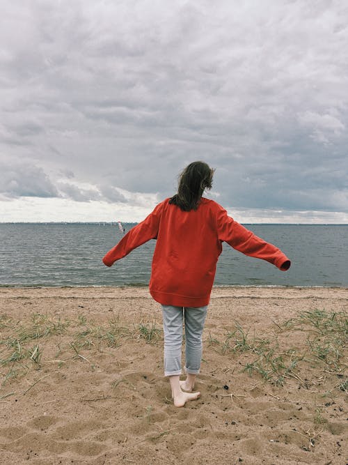 Woman in Red Long Sleeve Shirt  Standing on Brown Sand Near Water