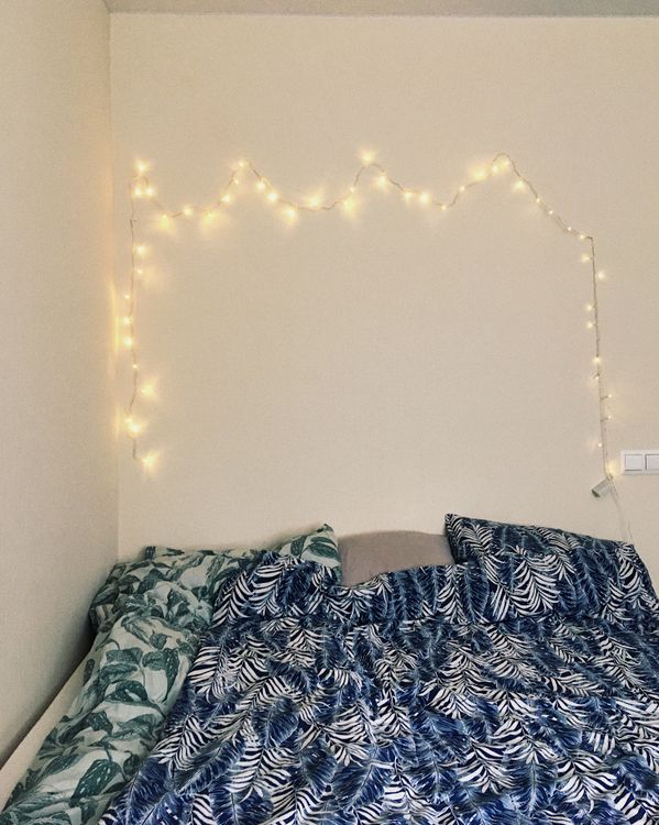 String lights glowing on a bedroom wall above botanical bedding