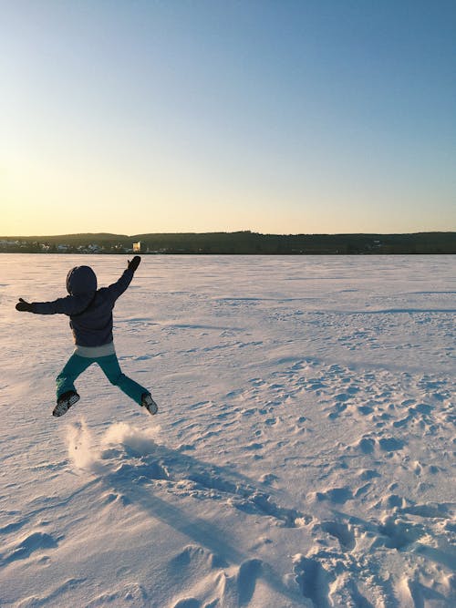 Free A Child in Black Jacket Jumping on Snow Covered Ground Stock Photo