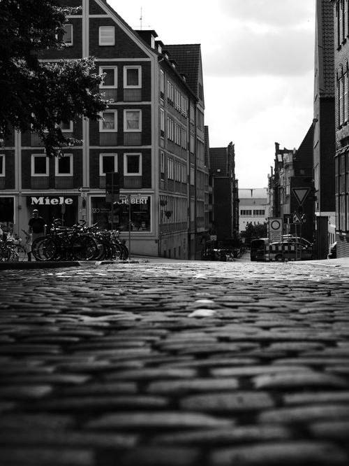 Free Black and white photo of a city street with cobblestones, bikes, and historic buildings. Stock Photo