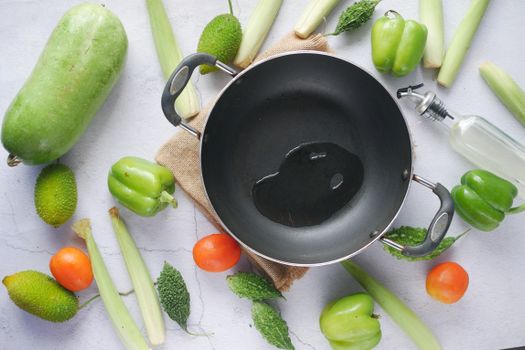 Top view of a wok surrounded by fresh vegetables and cooking oil, ready for meal preparation.