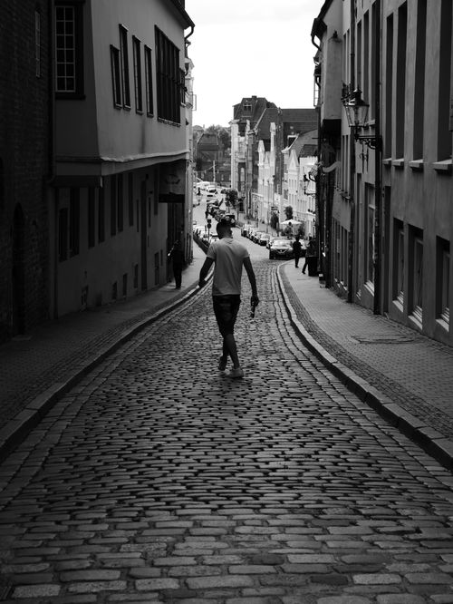 Free A person walks down a cobblestone street in a historic urban setting. Stock Photo