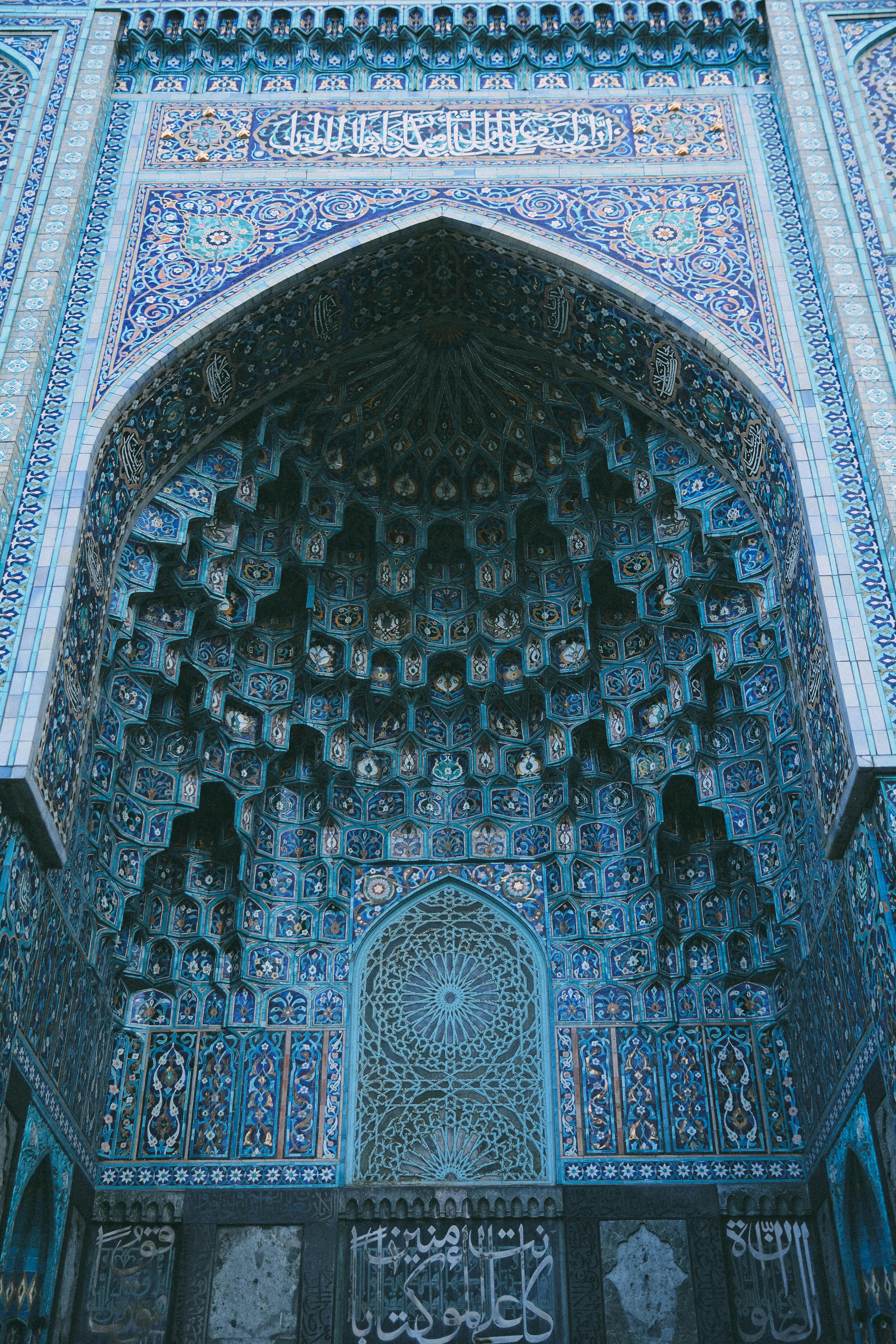 Vertical low angle view of ornate Islamic architecture with intricate blue mosaics and Arabic script.