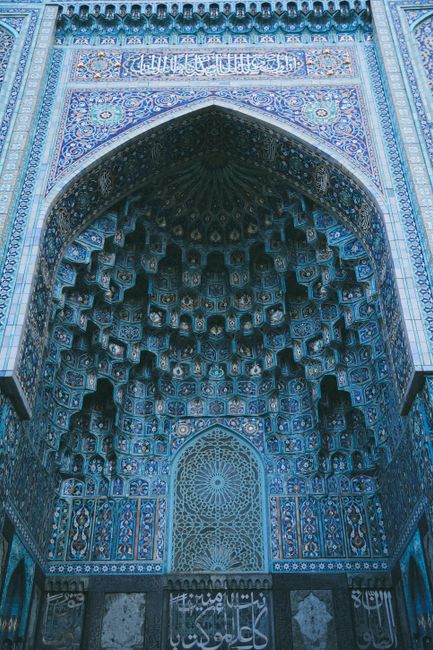 Vertical low angle view of ornate Islamic architecture with intricate blue mosaics and Arabic script.