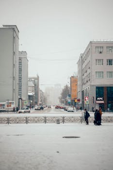 A snowy street surrounded by buildings on a cold winter day with people walking.