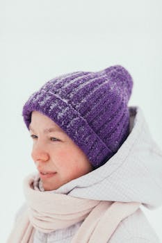 A cozy winter portrait featuring a person in a purple beanie amidst snowfall, evoking seasonal warmth.