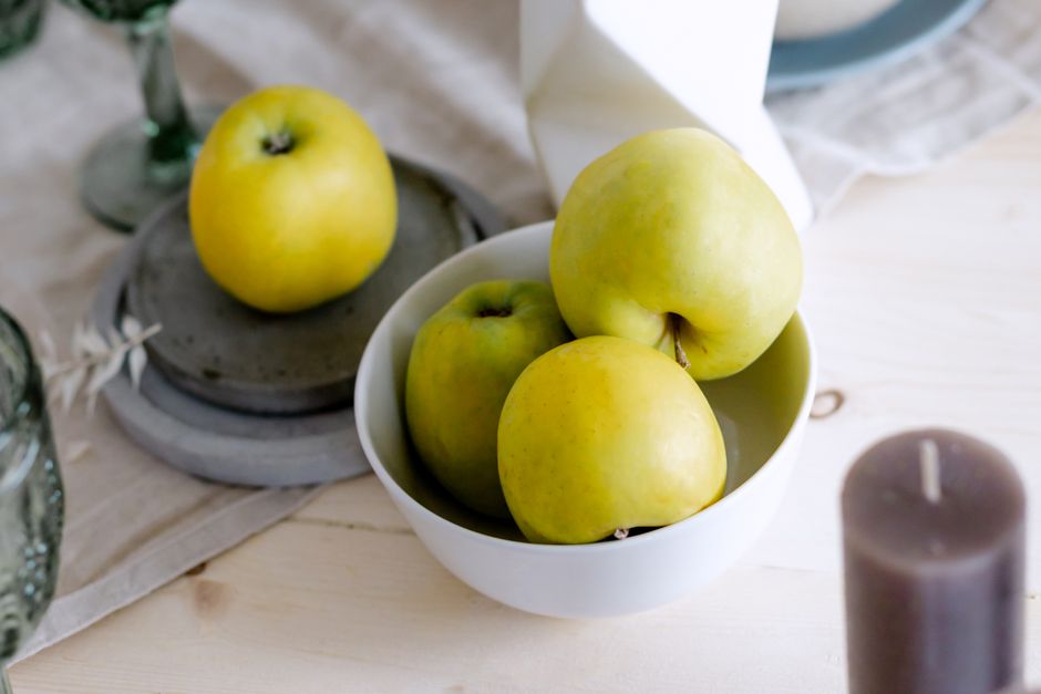 Close-up of fresh green apples in a white bowl on a table setting, perfect for healthy lifestyle themes.
