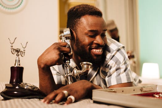 A cheerful man talks on a vintage rotary phone in a warm indoor setting.