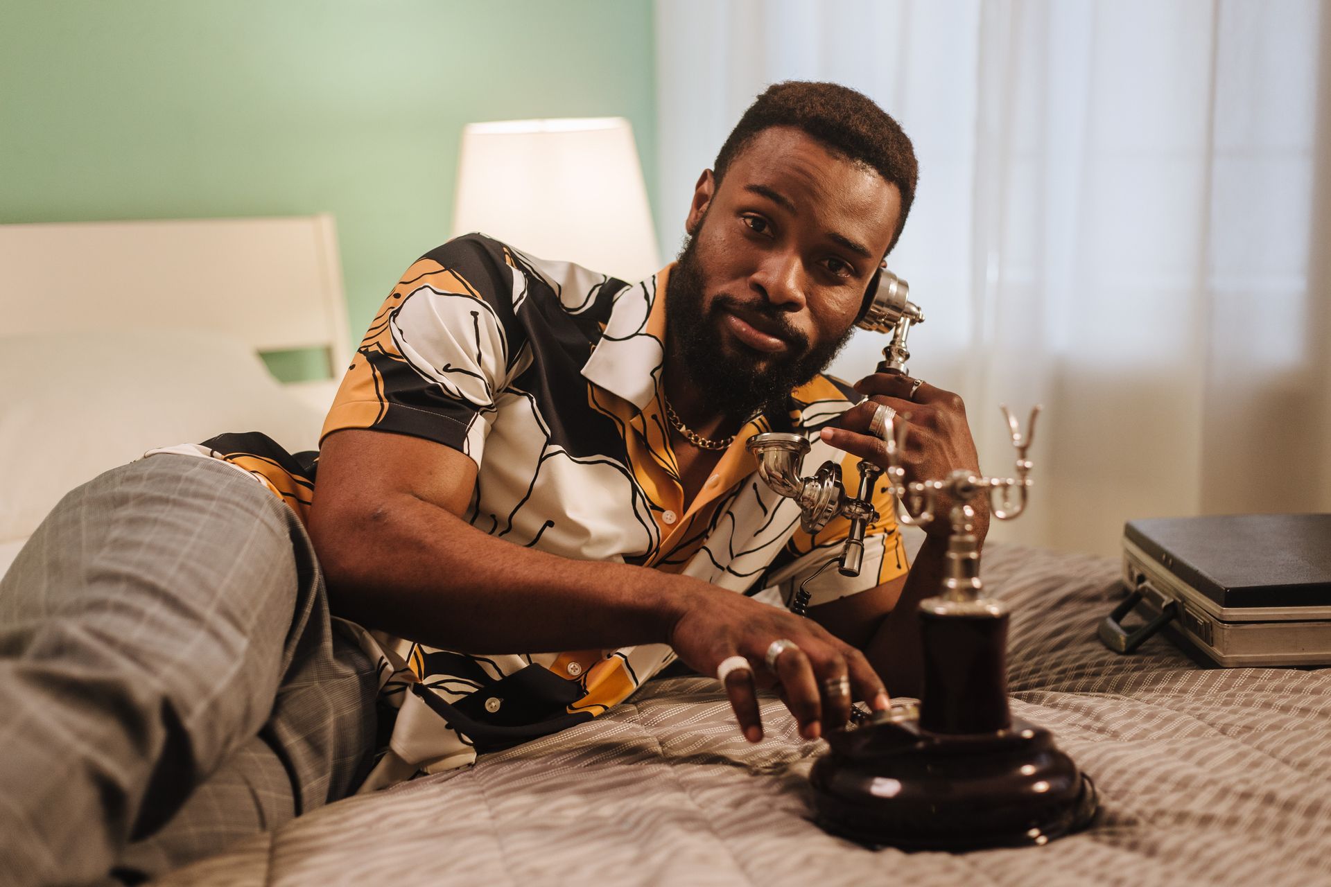 Man with vintage phone on bed in a stylish room. Perfect for lifestyle and interior themes.