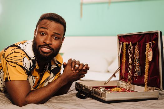 Bearded man showcasing assorted jewelries in a suitcase on a bed.