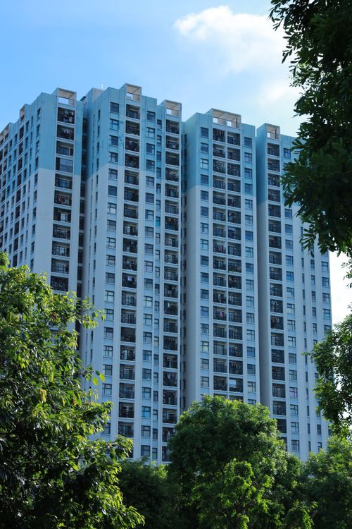 Free High-rise building standing tall against a clear sky with lush green trees. Stock Photo