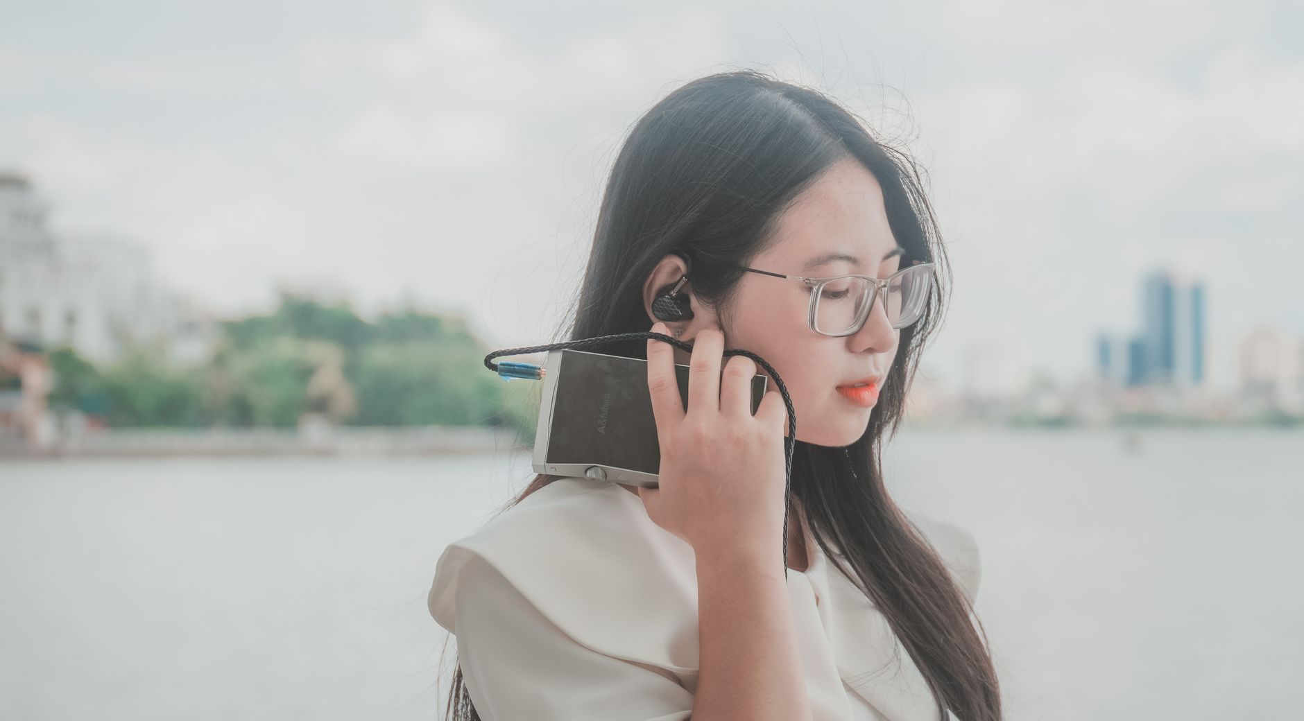 Side view of a young woman with eyeglasses listening to music through headphones outdoors on a sunny day.