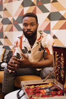 A fashionable man sitting indoors with modern geometric wallpaper and jewelry box.