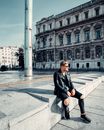 Woman in Black Leather Jacket and Black Pants Sitting on Sidewalk
