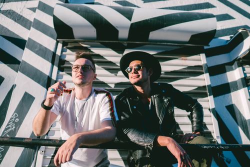 Free Two stylish friends enjoy a sunny day against a bold black-and-white Miami mural. Stock Photo