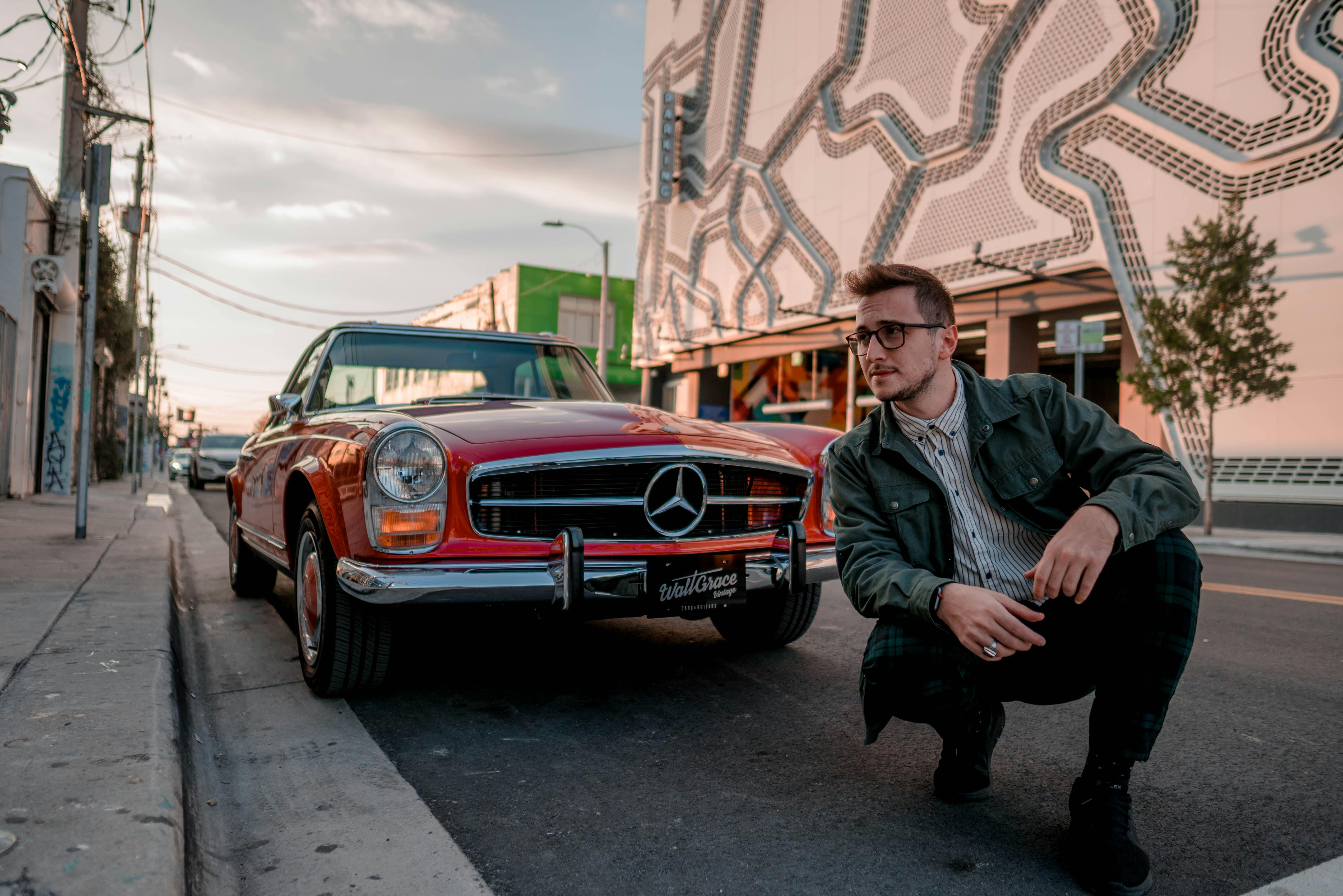 a man squatting in front of a red mercedes benz