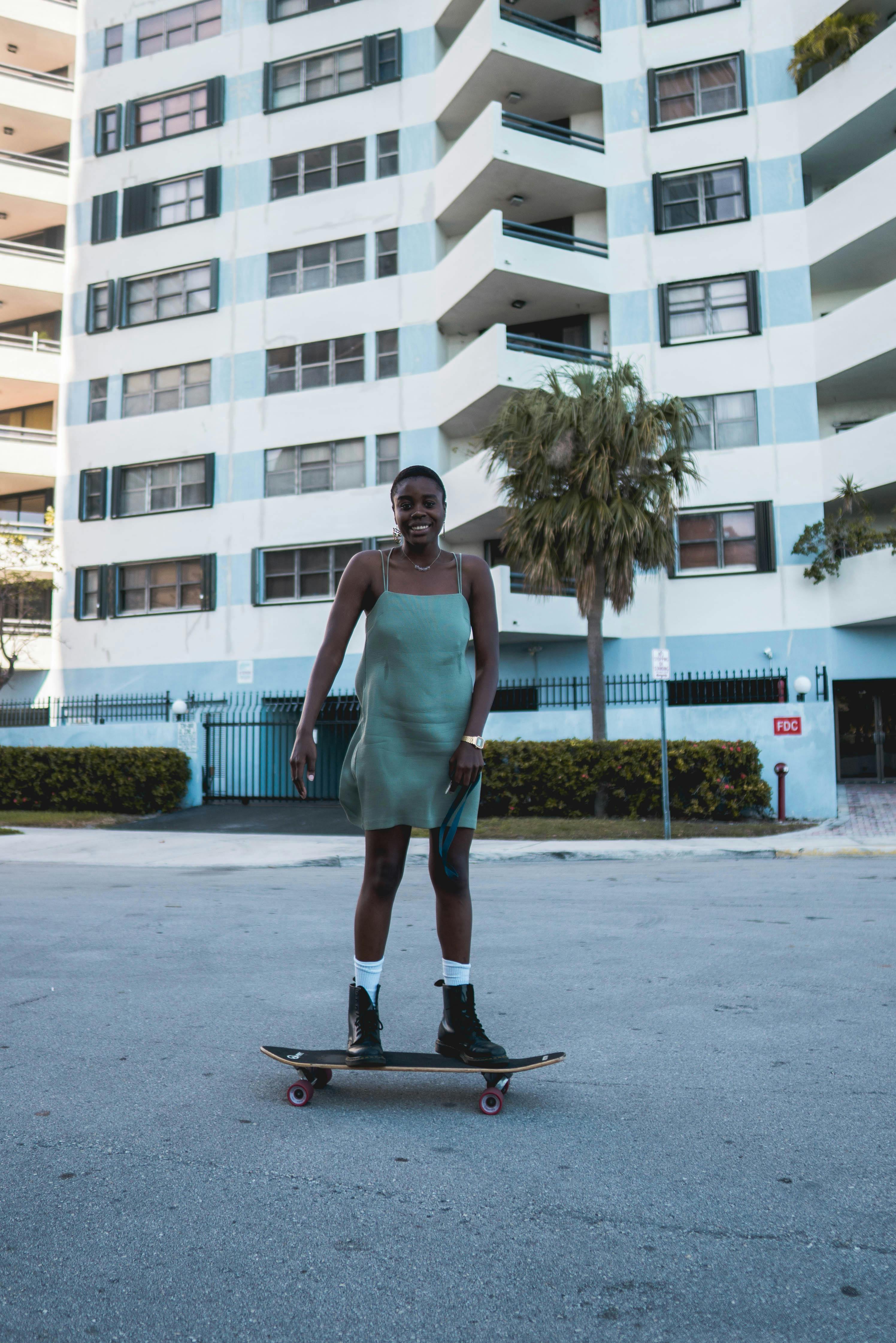 Young woman with short hair skateboarding outdoors in city setting, wearing a stylish dress.