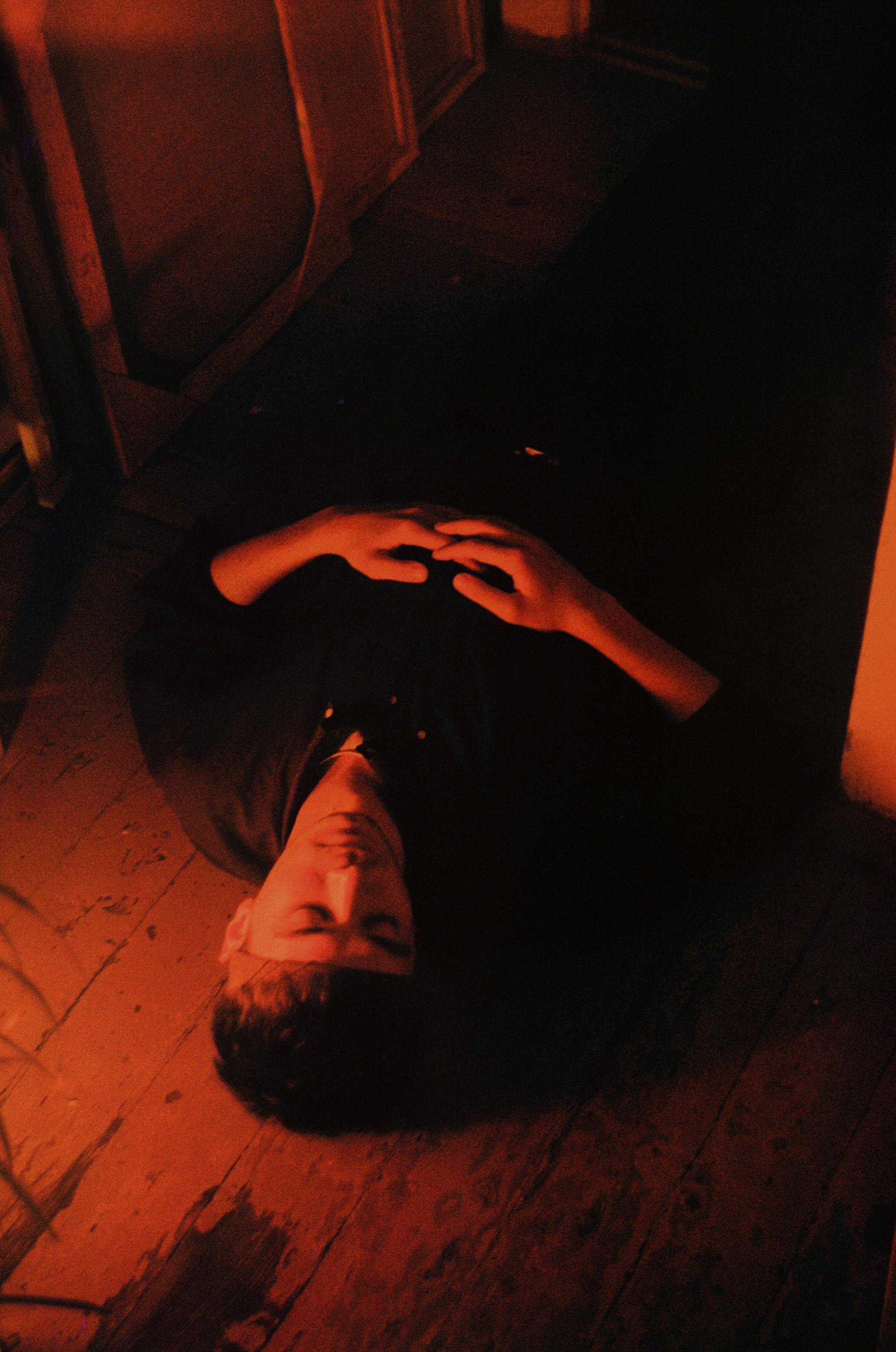 A moody, illuminated scene of a man lying down with eyes closed in low light.